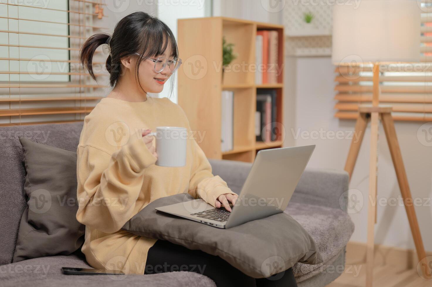 An attractive Asian woman is working remotely at home, sipping coffee, and working on her laptop. photo