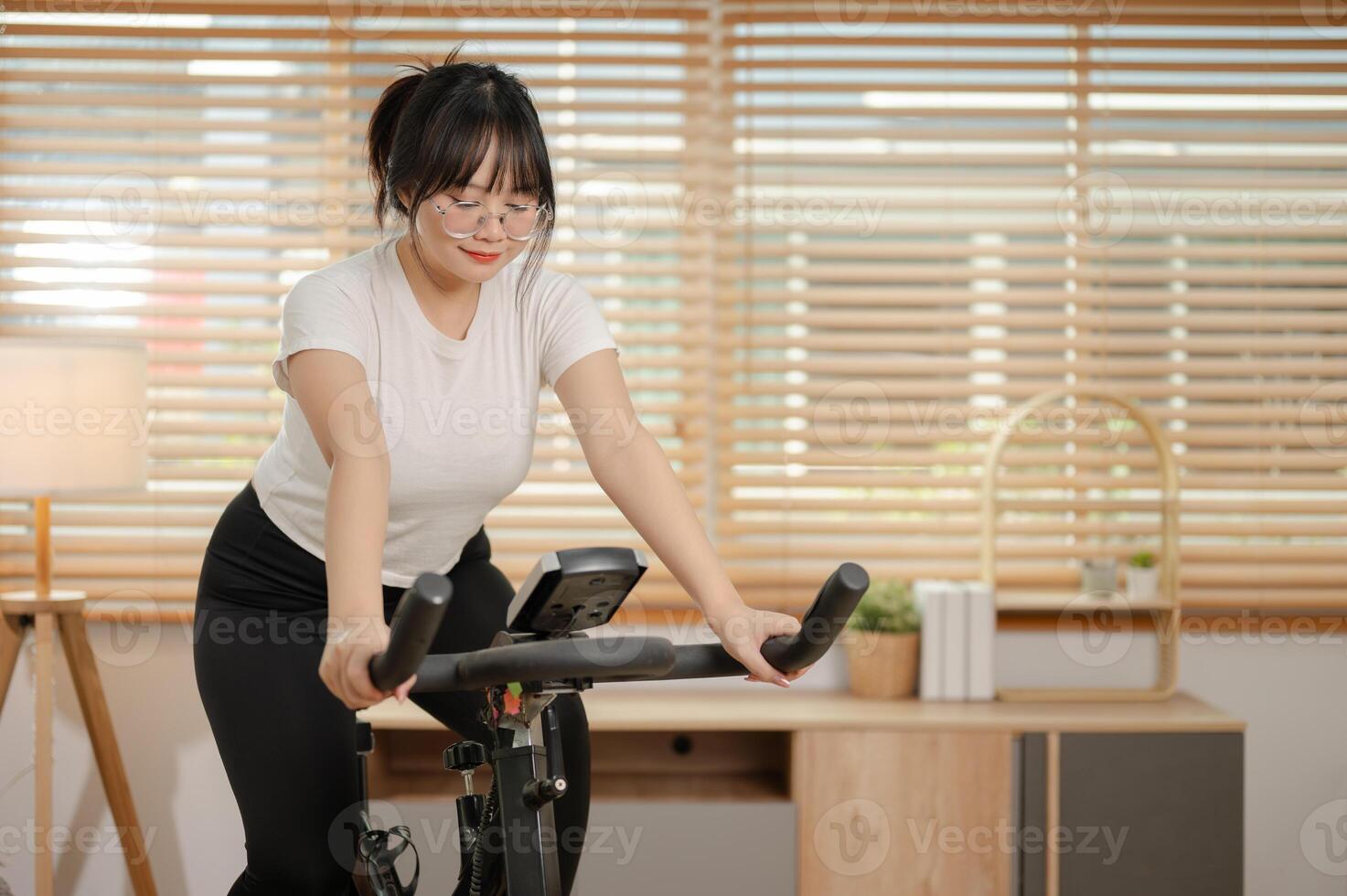 un saludable, ajuste asiático mujer en ropa de deporte es haciendo cardio a hogar, hacer ejercicio en un aptitud bicicleta. foto