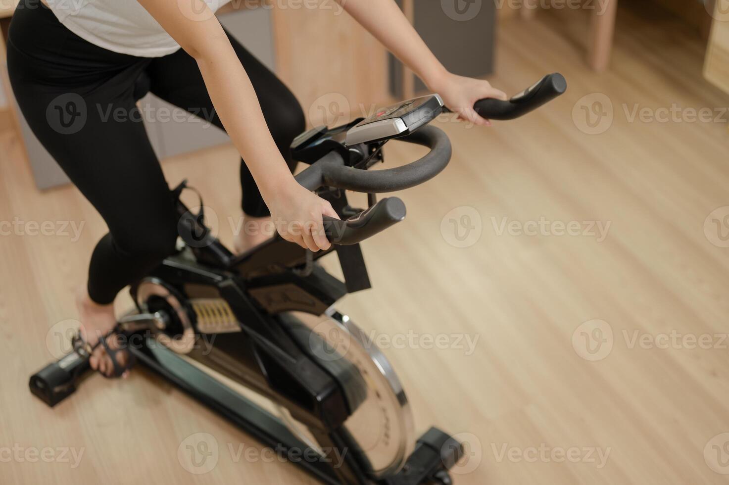 un recortado imagen de un mujer en ropa de deporte hacer ejercicio en un aptitud bicicleta, haciendo interior cardio a hogar. foto