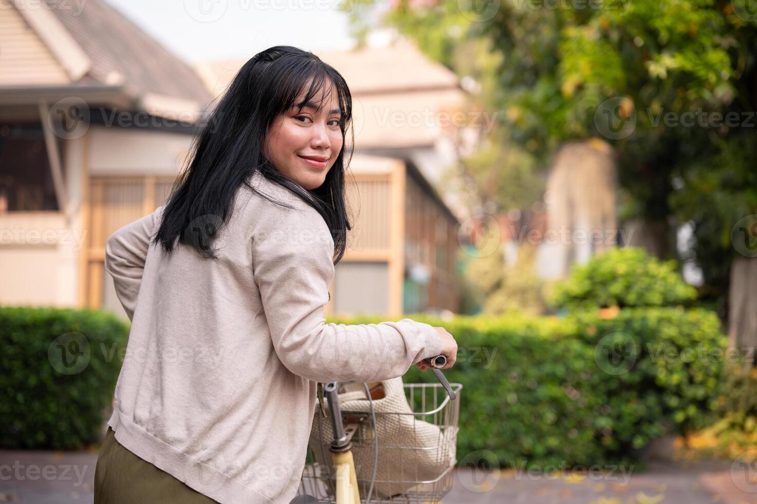 un sonriente, contento joven asiático mujer caminando y emprendedor su bicicleta en el ciudad. foto