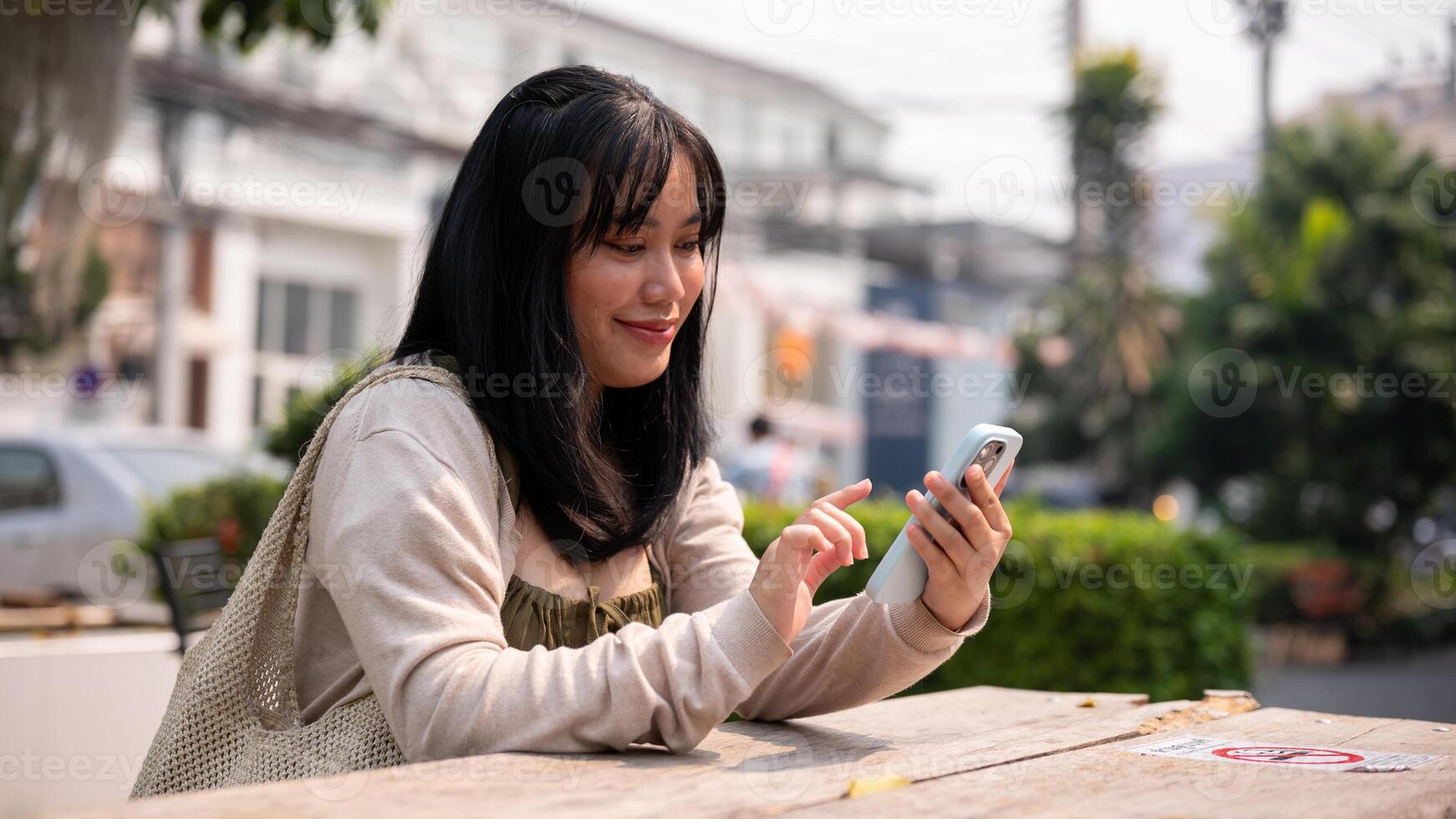 An attractive, happy Asian woman sitting at a table outdoors in the city and using her smartphone. photo