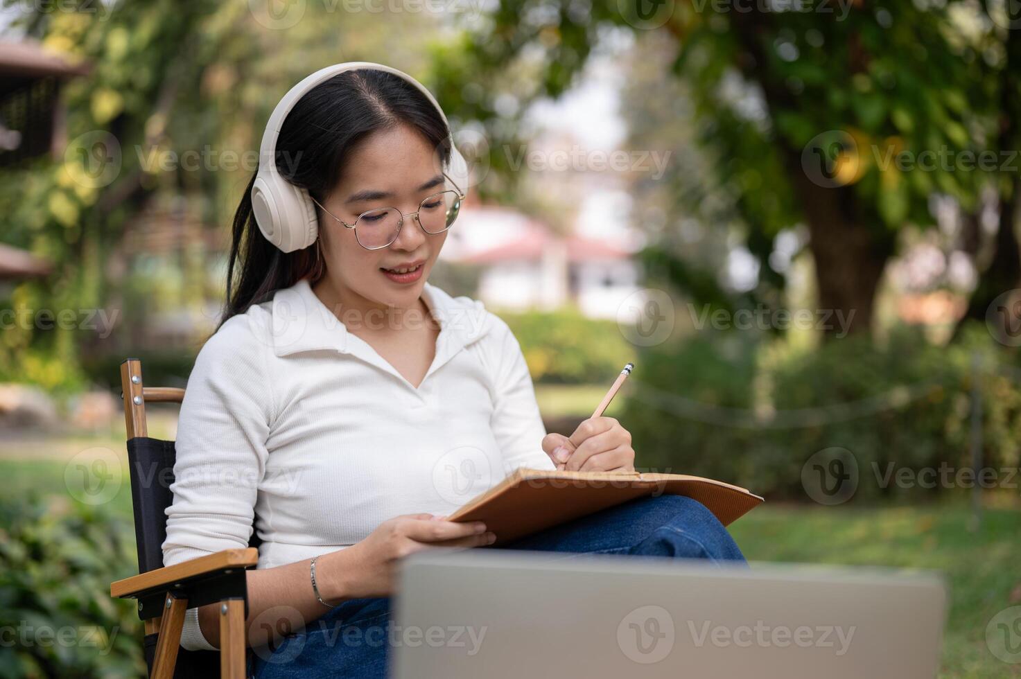 A young Asian woman is focusing on writing her work or keeping a diary while sitting in a backyard. photo