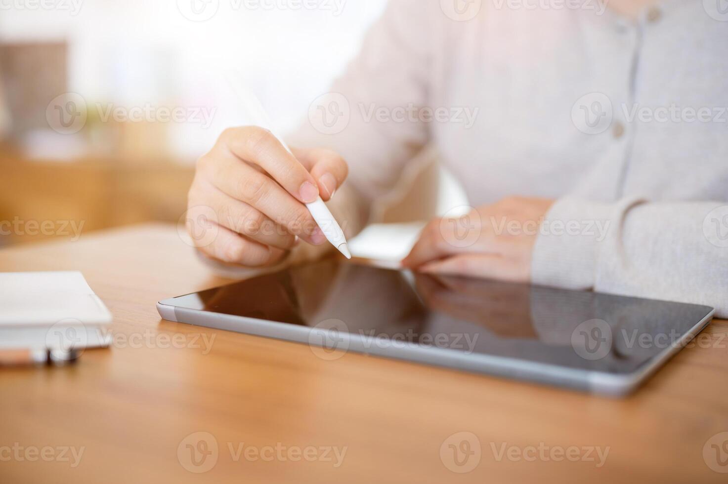 A cropped shot of a woman working on her digital tablet at a table indoors or in a minimalist cafe. photo