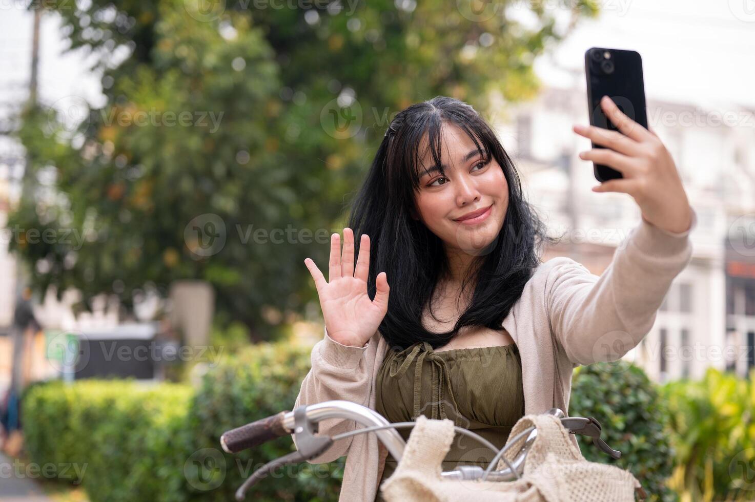A happy Asian female traveler is taking selfies while exploring the city with her bike. photo