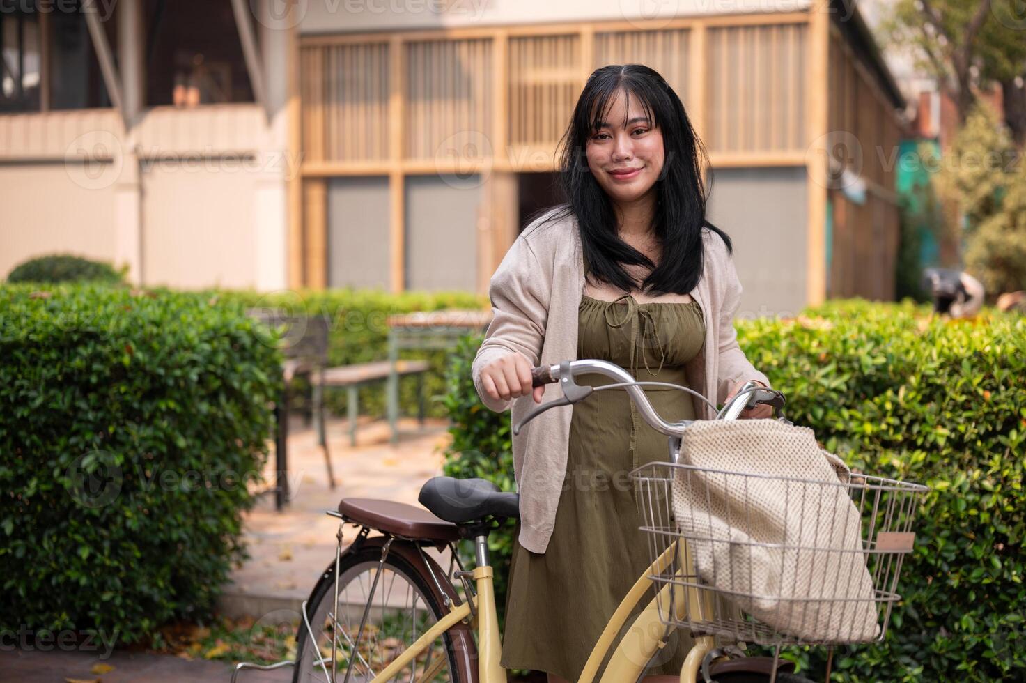 A smiling young Asian woman in a cute dress with her bicycle in the city on a sunny day. photo