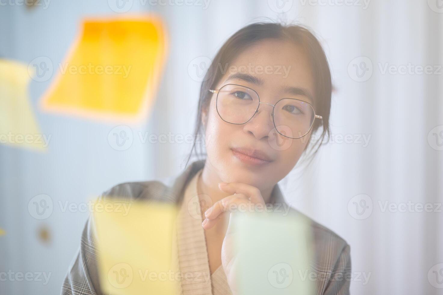 A positive Asian businesswoman brainstorming with her team, reading ideas on sticky notes. photo