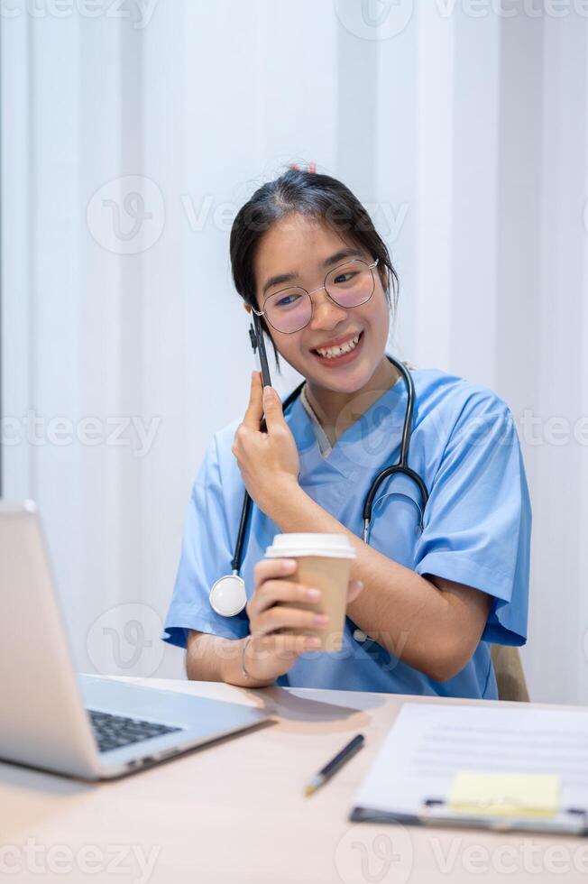 un trabajo duro asiático hembra médico es hablando en el teléfono mientras leyendo médico casos en ordenador portátil. foto