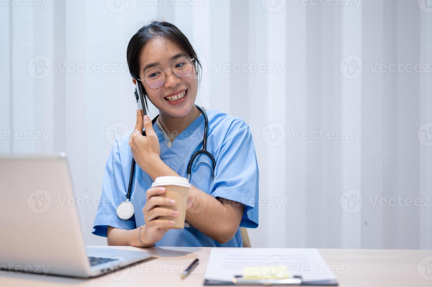 A hardworking Asian female doctor is talking on the phone while reading medical cases on laptop. photo