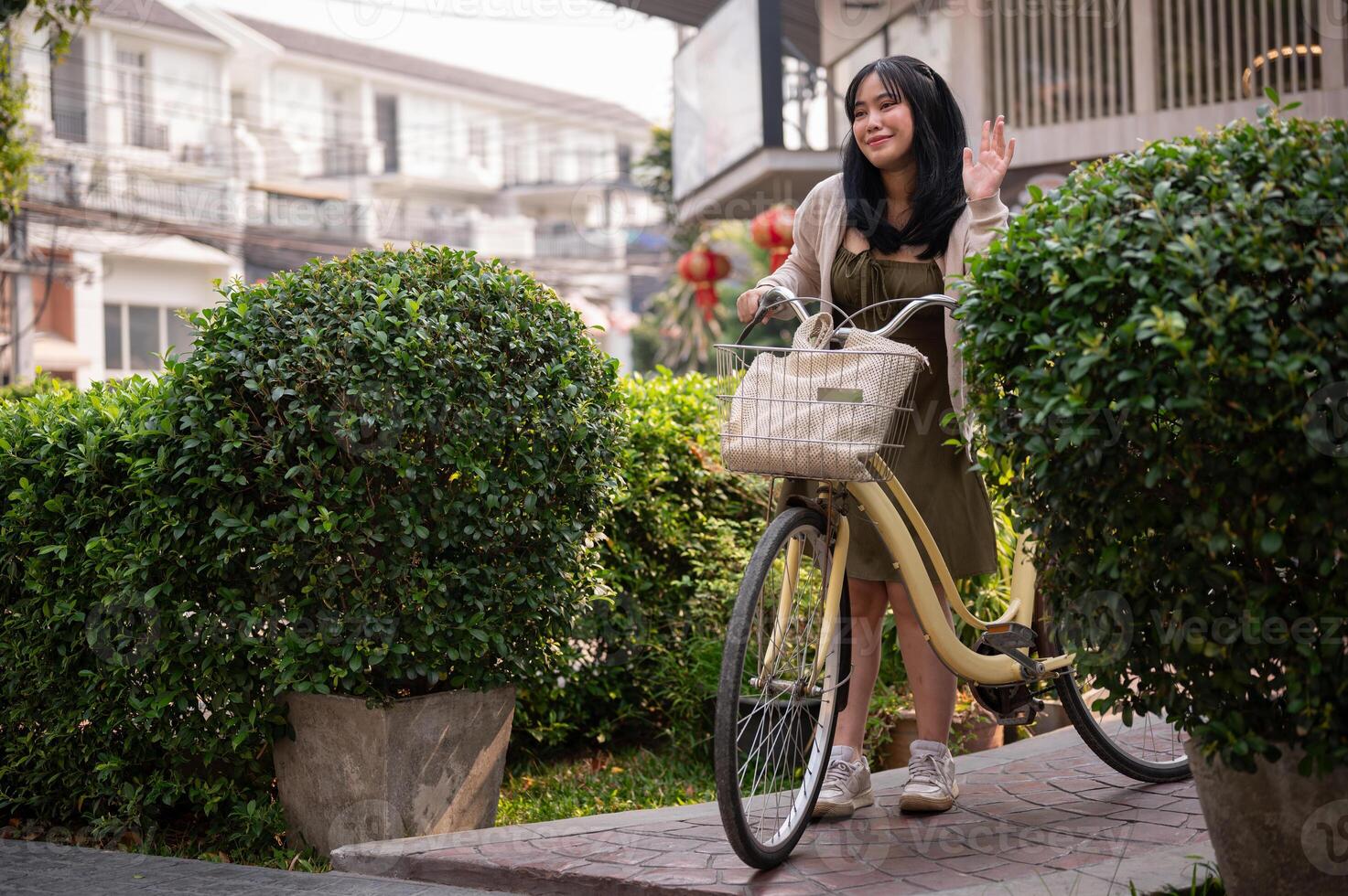 un simpático asiático mujer olas su mano a decir Hola a su amigo mientras emprendedor su bicicleta en el ciudad. foto