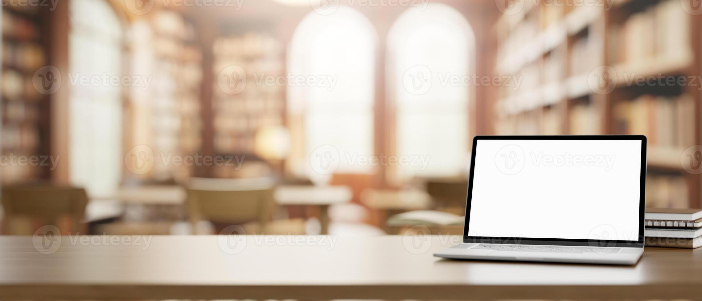 A white-screen laptop computer mockup and books on a wooden table in a beautiful vintage library. photo