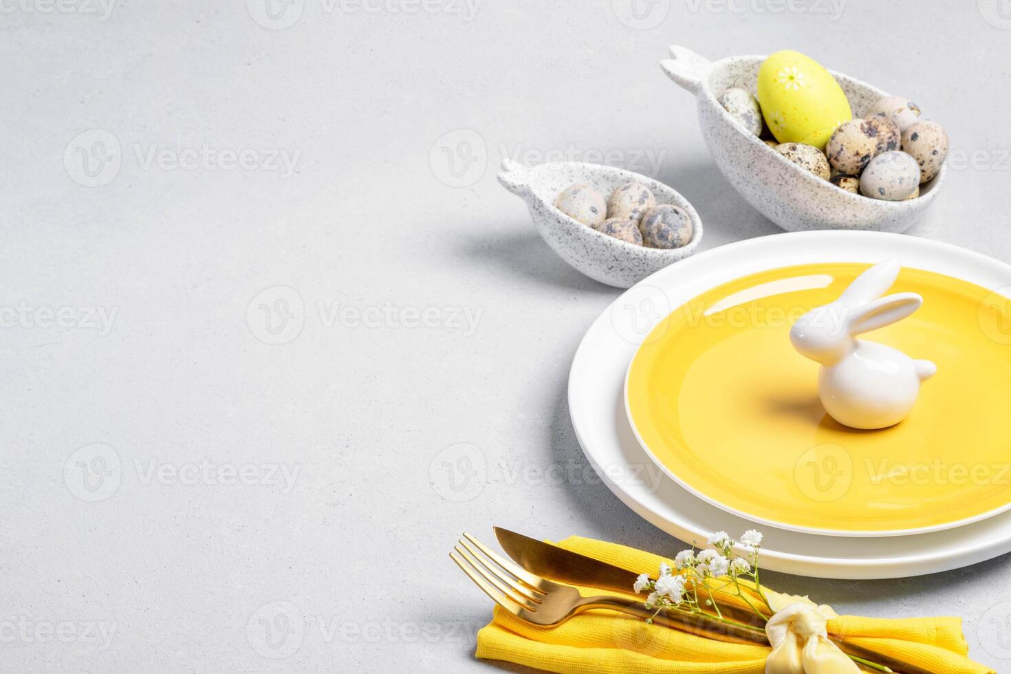 Easter table serving. White yellow dishware, quail eggs, golden cutlery, white ceramic bunny on gray photo