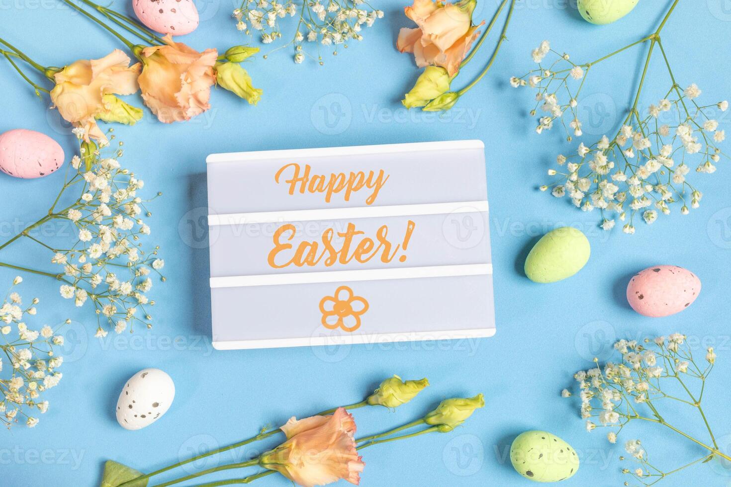 Inscription Happy Easter surrounded by decorative eggs, white and peach flowers on blue. Top view. photo