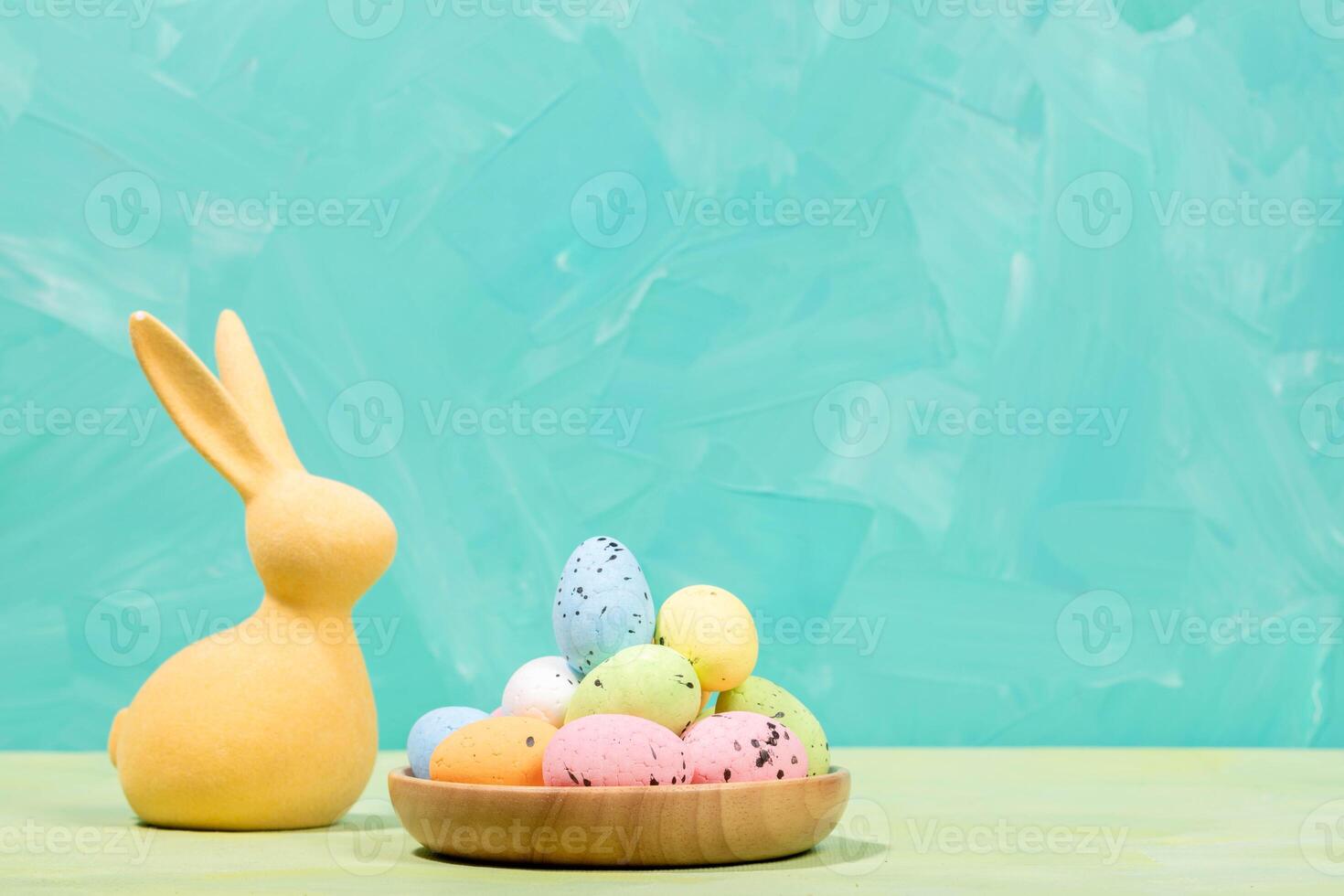 Easter card. Yellow bunny and decorative colorful eggs in wooden plate on turquoise Copy space. photo