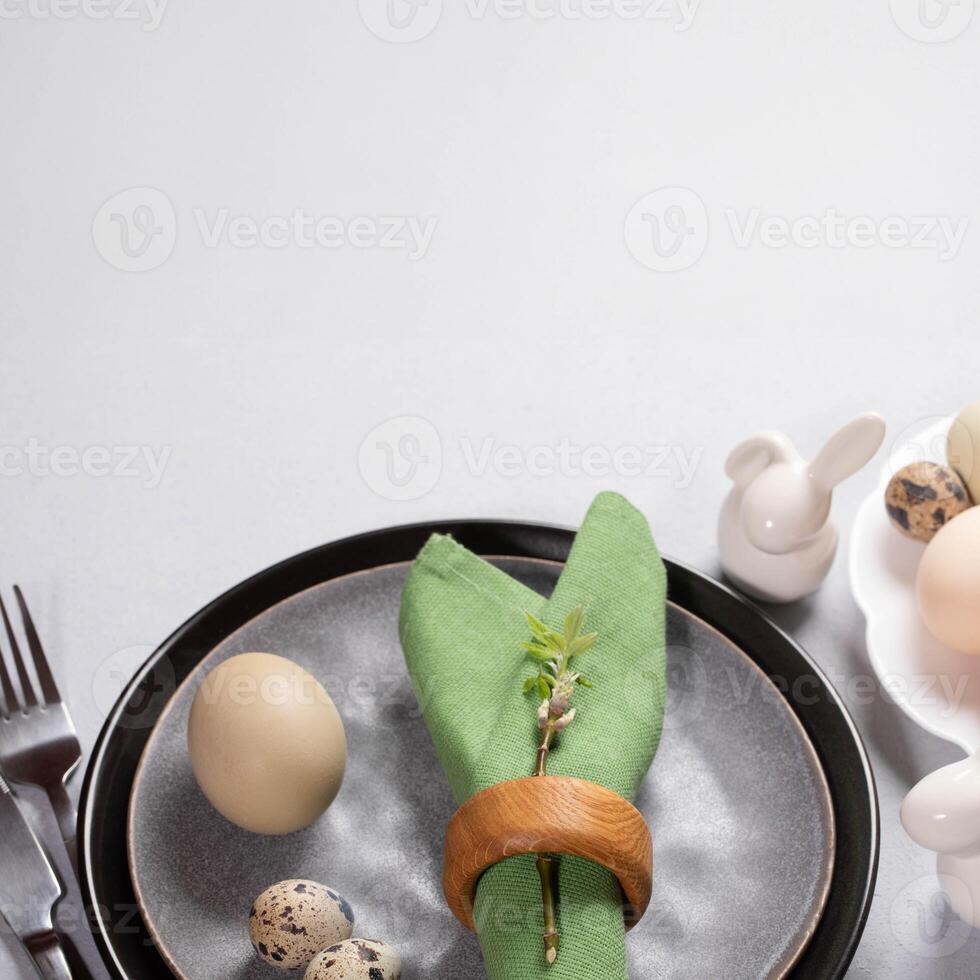 Easter table in trendy natural colors. Gray plates, green napkin, organic eggs, ceramic bunnies. photo