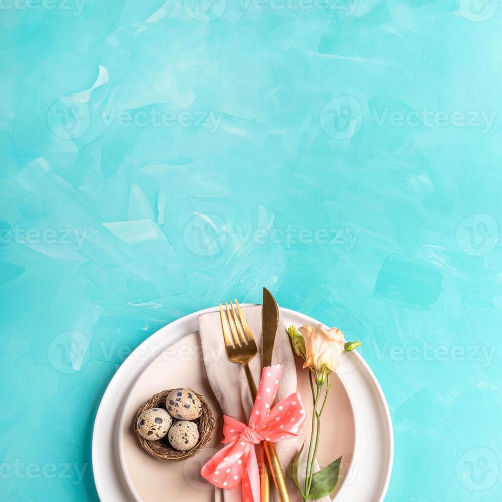 Easter. Top view. Beige plates, nest, quail eggs, golden cutlery, flower on turquoise. Copy space. photo