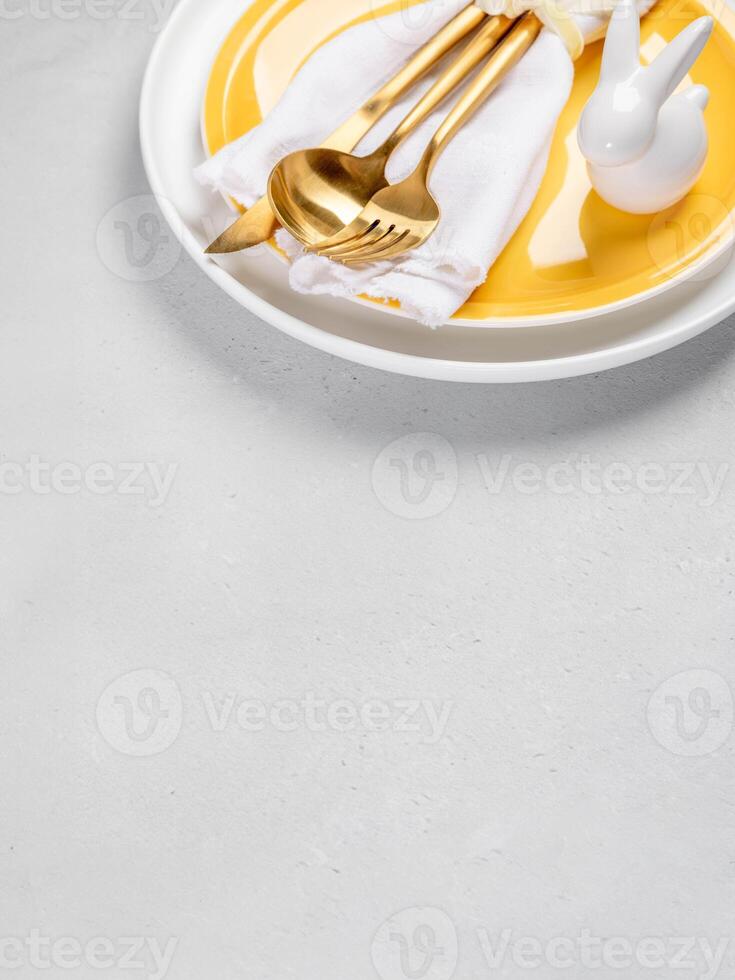 Card for Easter menu. Yellow and white plates, white napkin, gold cutlery, ceramic bunny. Copy space photo