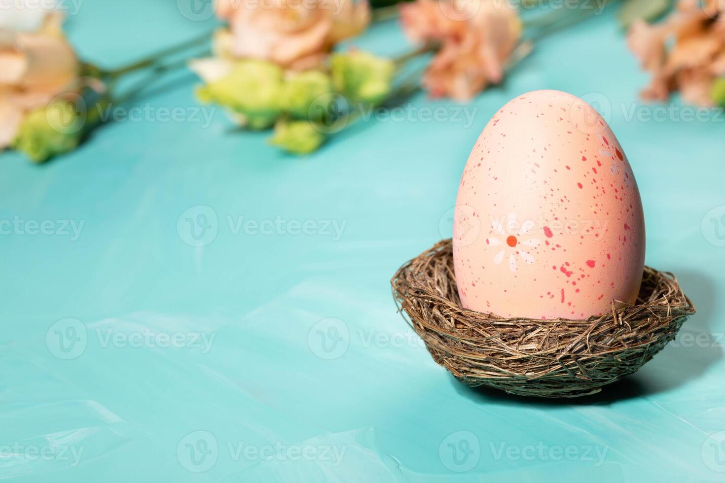 Decorative pink Easter egg in nest, peach Eustoma flowers on turquoise. Easter card. Copy space. photo