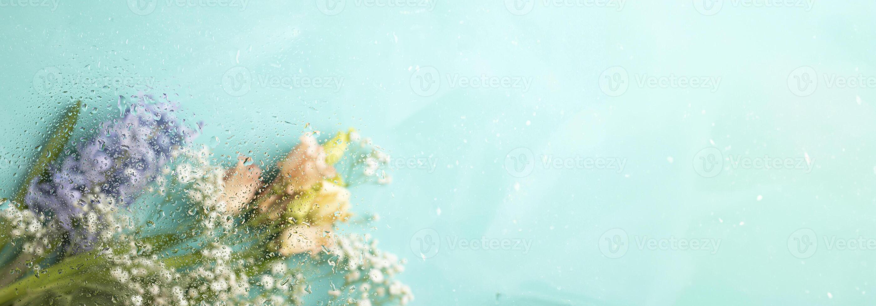 Banner for spring holiday. Blurred flowers on turquoise. Shot through wet glass. Copy space. photo