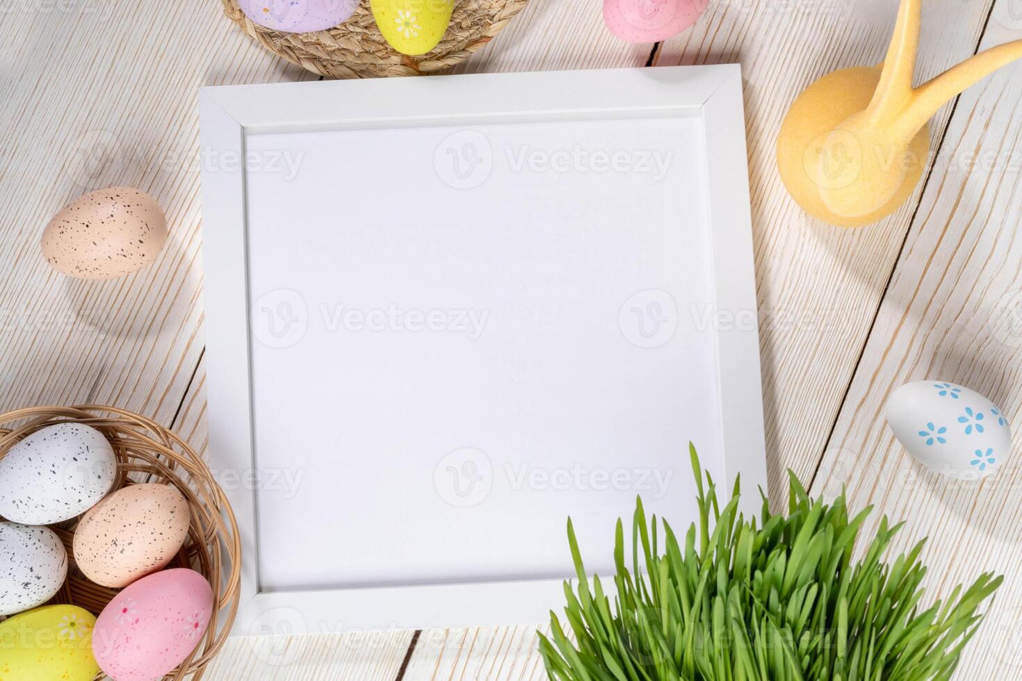 Easter layout. White frame, decorative color Easter eggs, yellow bunny, green grass on wooden table. photo