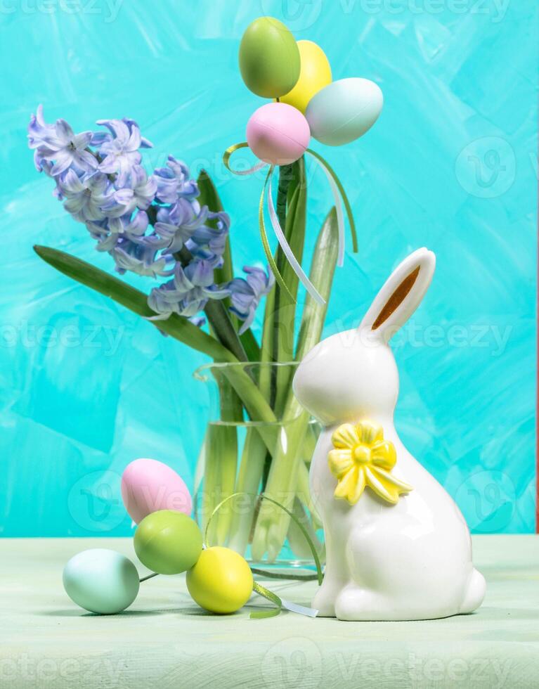 Easter color decorative eggs, white ceramic bunny, purple jacinth flower on turquoise backdrop. photo