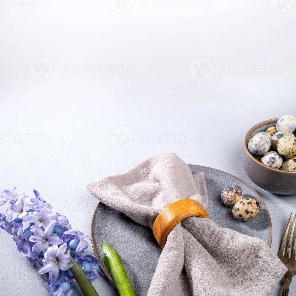 Easter table serving. Gray tableware, gray napkin, quail eggs, jacinth flower on neutral. Copy space photo