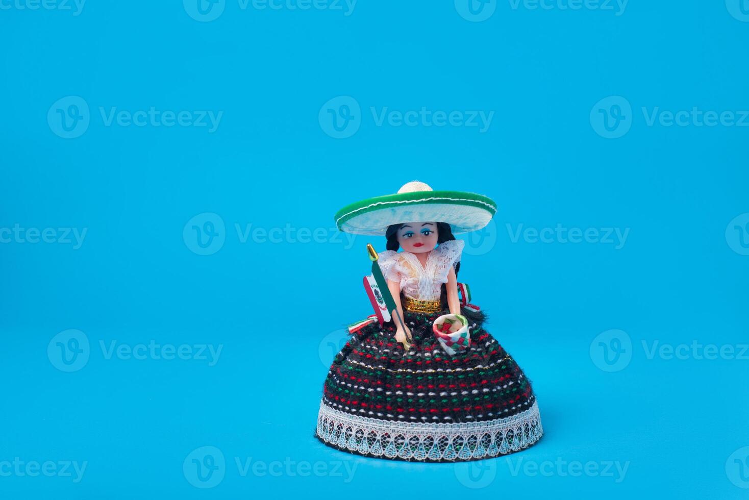 Small doll representing a Mexican woman with hat and Mexican flag. Isolated figure on blue background. photo