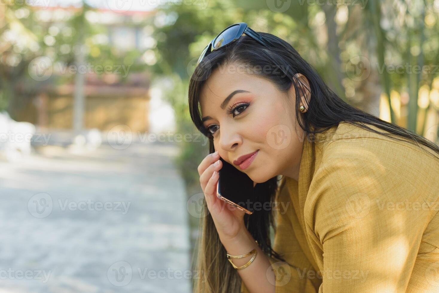 mujer sentado en un parque banco hablando en el teléfono. soleado día. foto