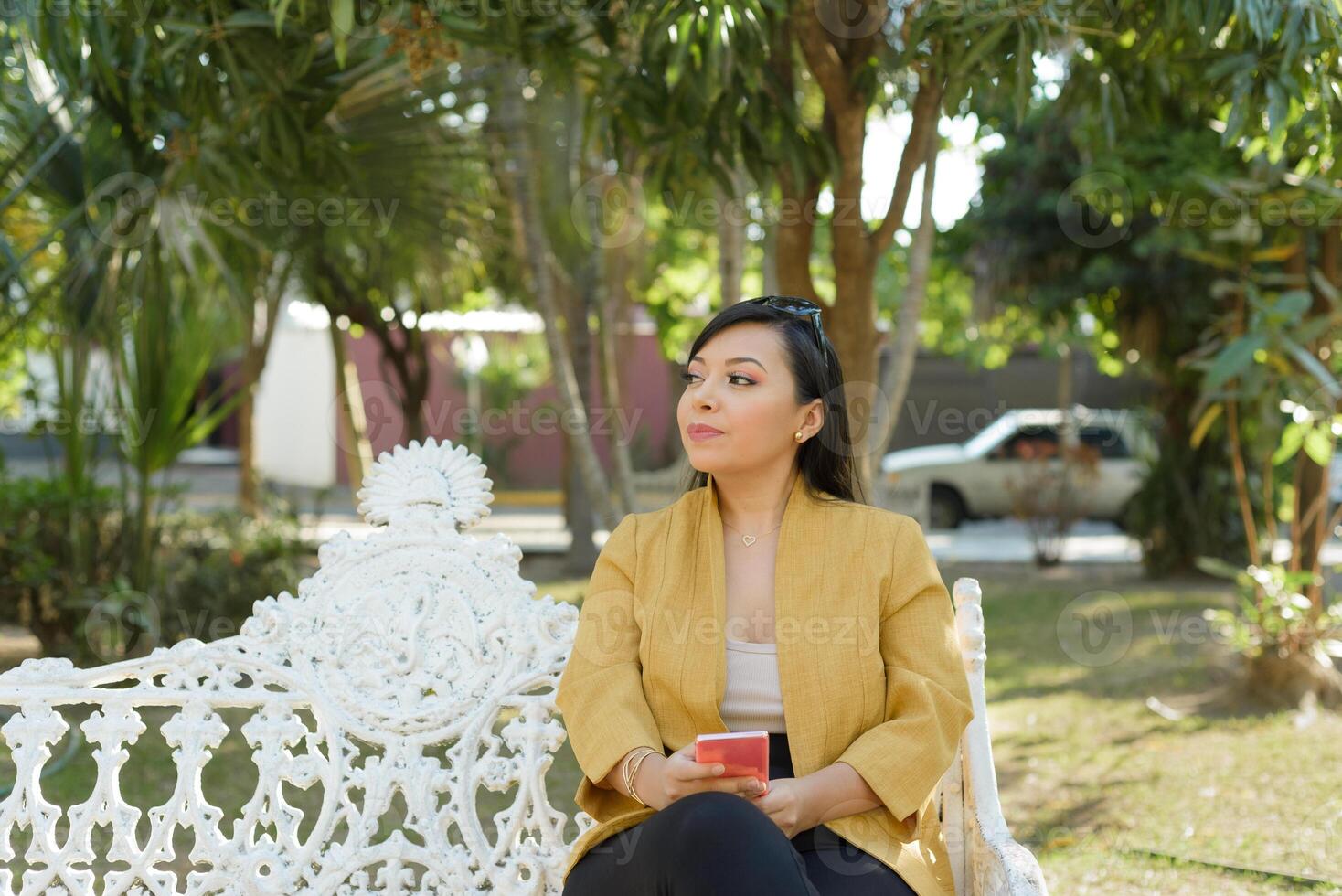 Woman sitting on a bench in a garden using her cellphone. photo