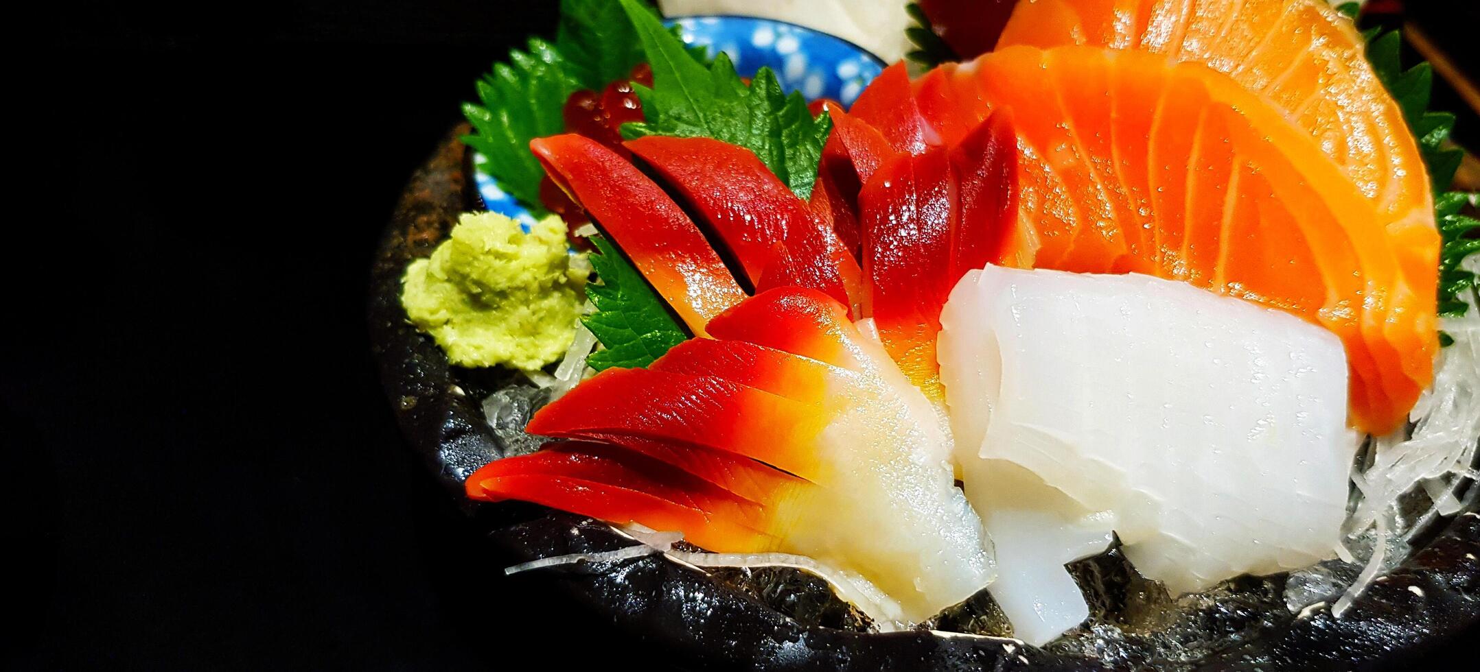 Fresco sashimi en negro plato a japonés alimento. muchos rebanadas de pez, salmón y atún con wasabi asiático comida estilo. foto