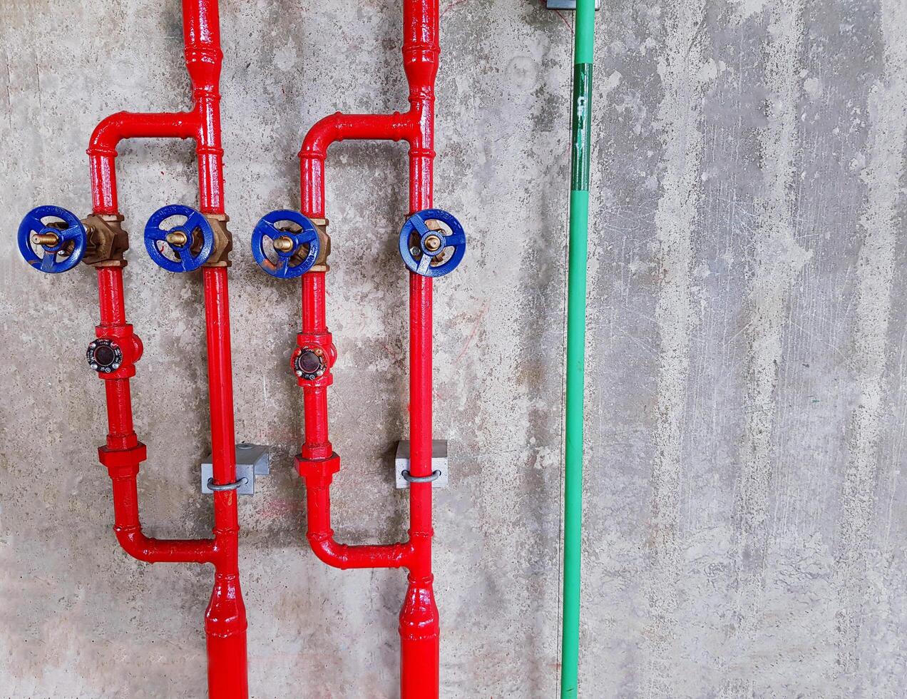 Red water and green pipe line with four blue water valves installed on gray rough concrete wall background with copy space. Industrial and System installation concept photo