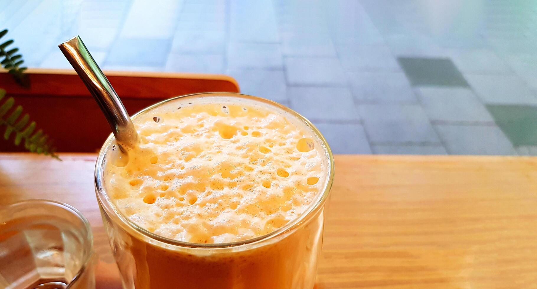 Close up iced caramel macchiato frappe with cold water on wooden table with copy space at cafe shop. Refreshment drinking concept. photo