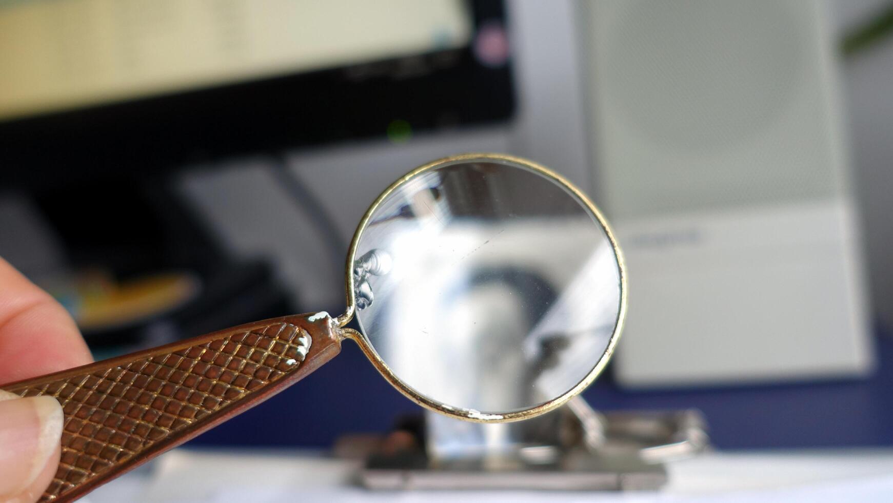 A antique magnifying glass held between the thumb and forefinger photo