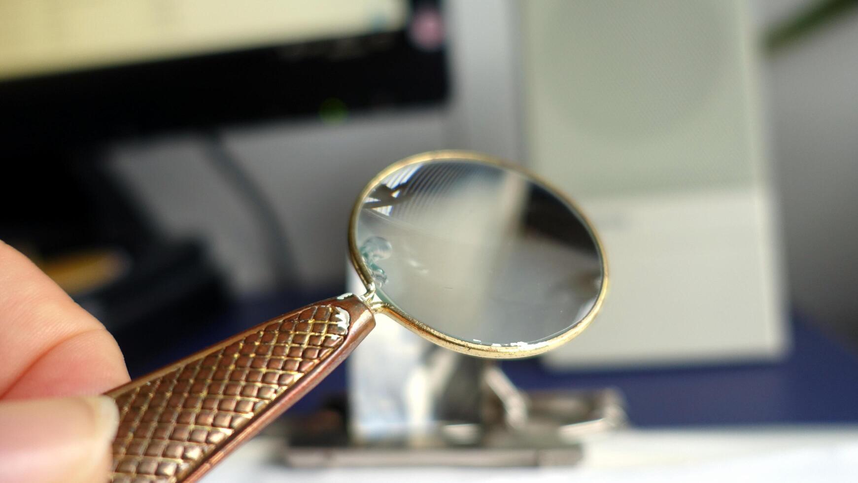 A antique magnifying glass held between the thumb and forefinger photo