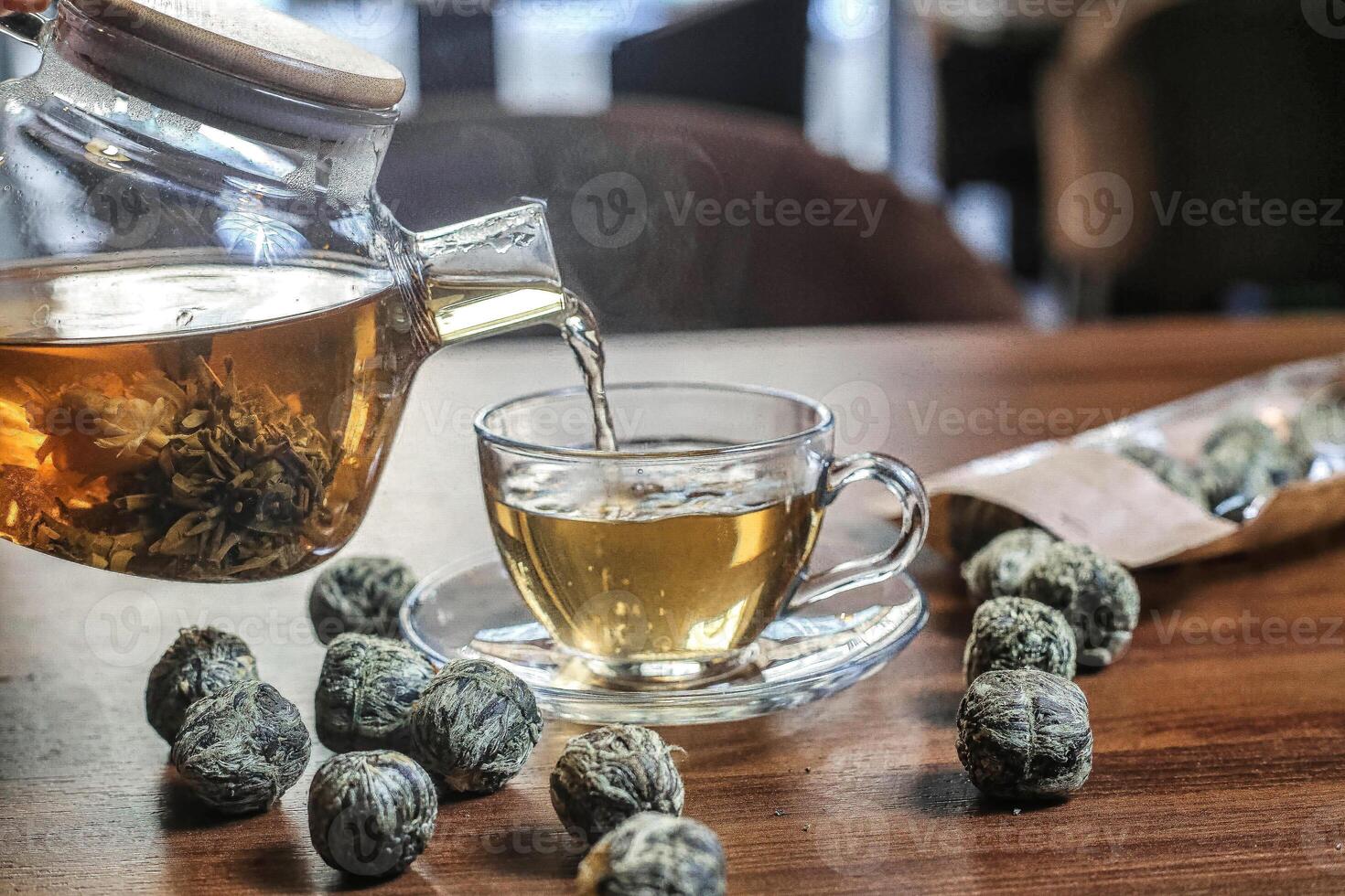 Pouring a Cup of Tea Into a Glass Teapot photo
