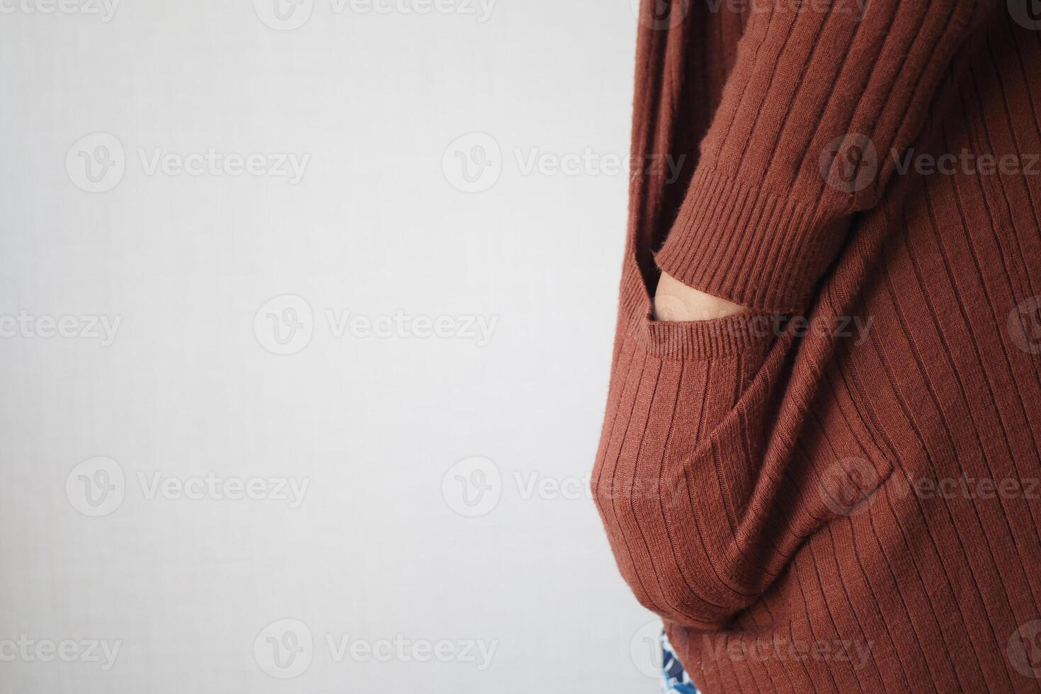 A woman in a brown sweater is standing with hands in pockets photo