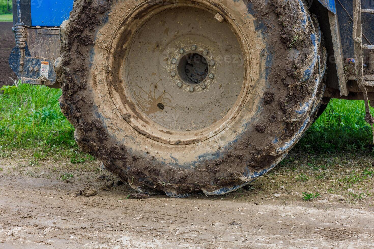 dirty double wheel of a big agriculture tractor on dirt road at summer day photo