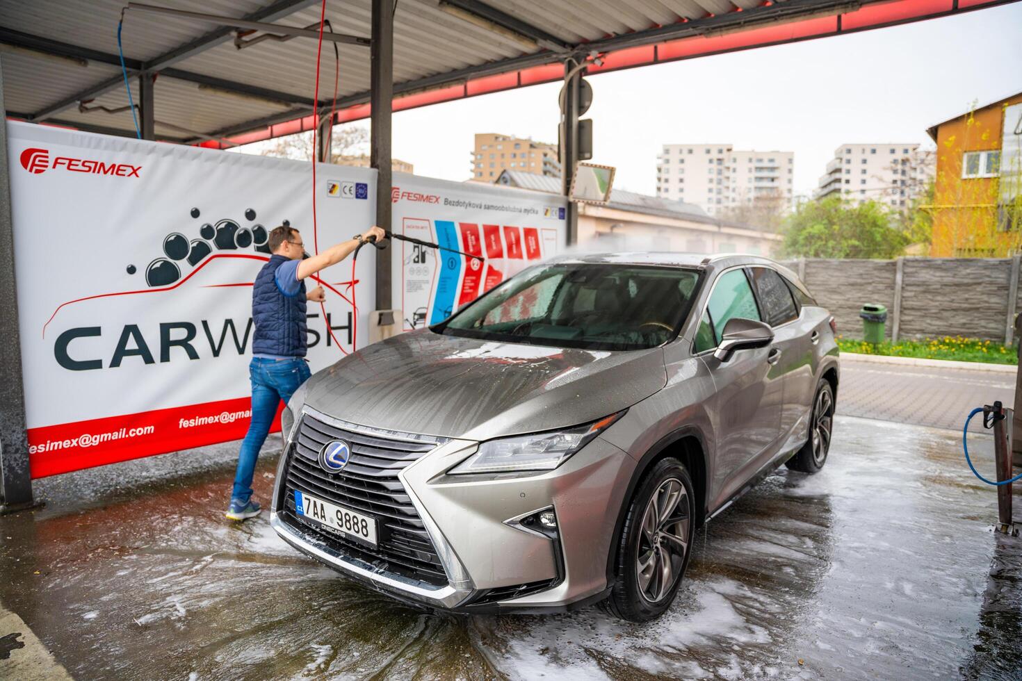 Prague, Czech Republic - April 5, 2024. Young man washes his car at a self-service car wash using a hose with pressurized water and foam. High quality photo