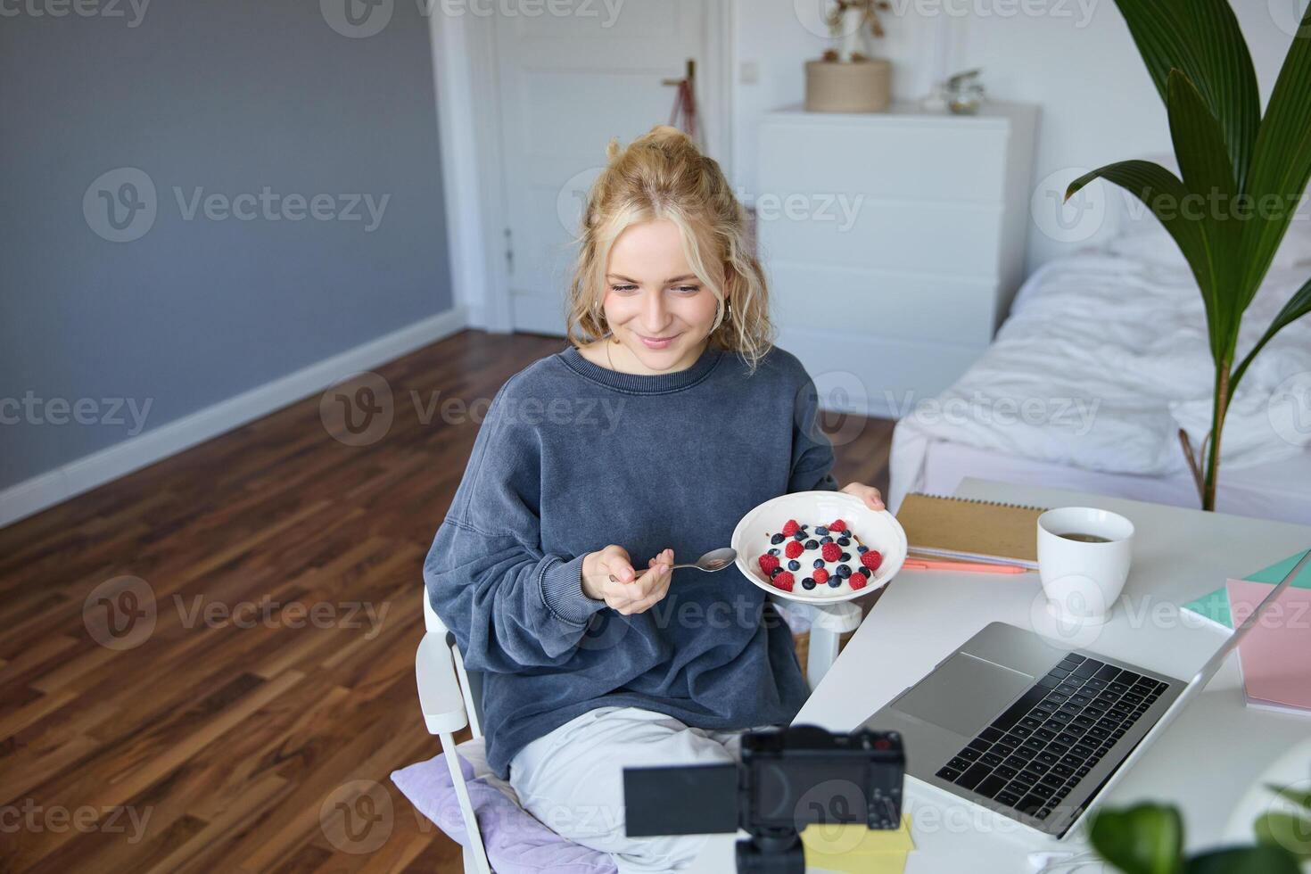 Portrait of young woman vlogger, recording herself while eating homemade healthy breakfast, creating vlog content for followers photo