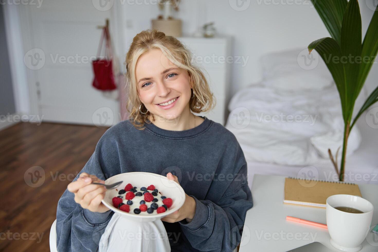Cute girl eats breakfast and drinks tea in her room, makes herself healthy lunch in bowl, sits in bedroom photo