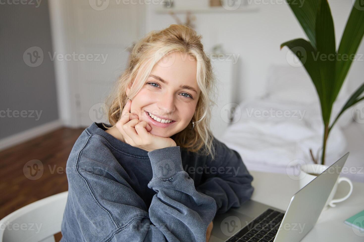 Close up portrait of young smiling female model, sits in a room with laptop, works from home, does online course, e-learning photo