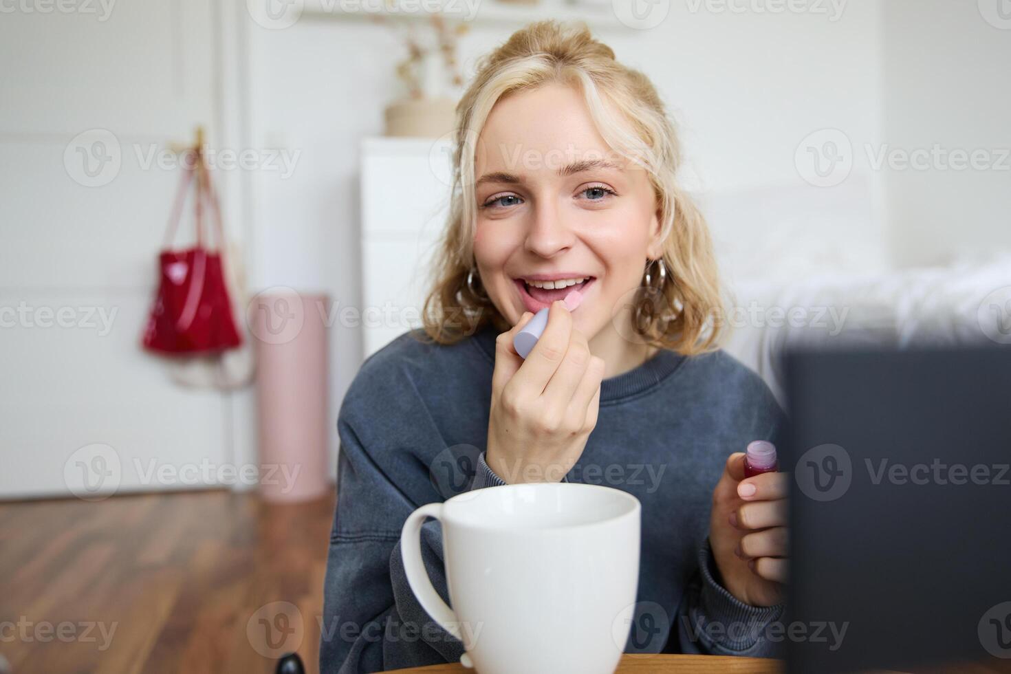 Lifestyle, beauty blogger, woman recording of her putting on makeup, talking to camera, making online tutorial, showing her lip gloss or lipstick to followers, sitting on floor with cup of tea photo