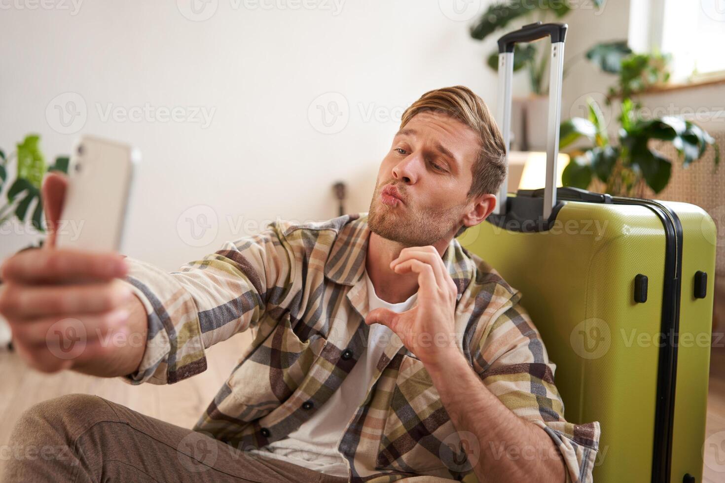 Handsome smiling man shows kissing face and heart sign, goes on holiday, takes selfie on mobile phone app photo