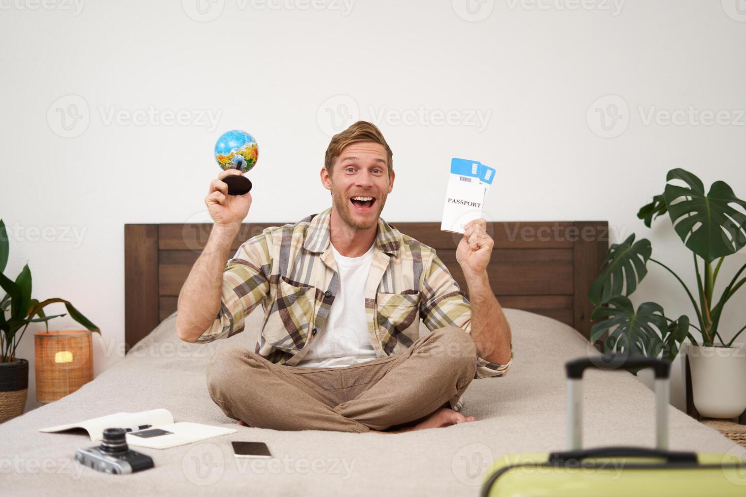 retrato de alegre, contento turista, hombre sentado con avión Entradas y un globo, lleno maleta para de viaje alrededor el mundo, yendo en vacaciones, emocionado acerca de su fiesta foto