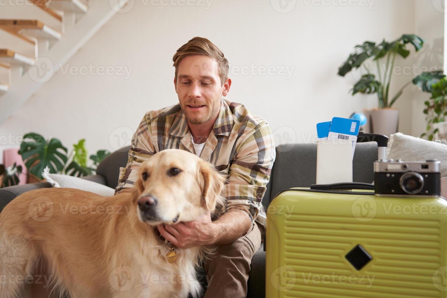 Portrait of young man, traveller, pets his dog, sits with suitcase and tickets, goes on holiday photo