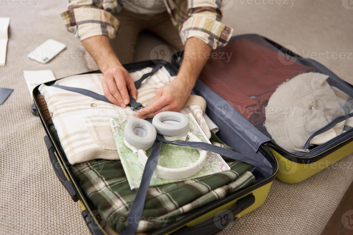 Close up of male hands, man fastening clothes inside suitcase, packing his belongings in luggage, going on holiday, travelling photo