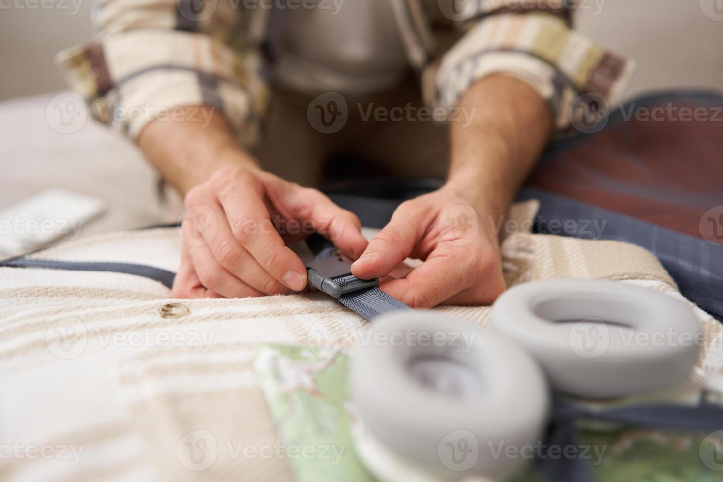 Close up of male hands, man fastening clothes inside suitcase, packing his belongings in luggage, going on holiday, travelling photo