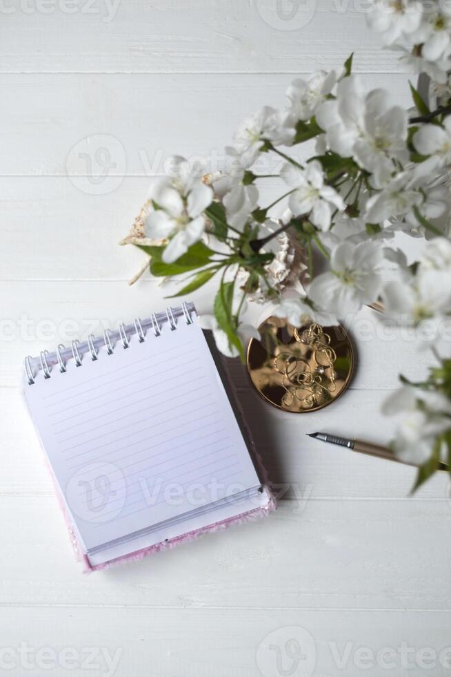 Opened notebook and spring flowers on a white wooden desk. photo