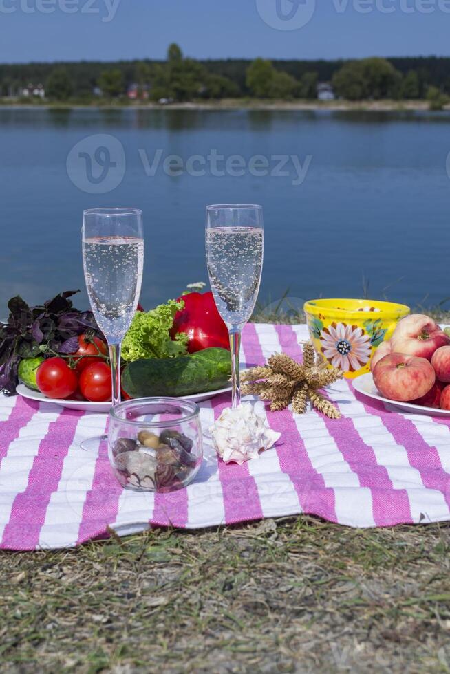 Beautiful picnic with fruits, vegetables and glasses of wine near lake. photo