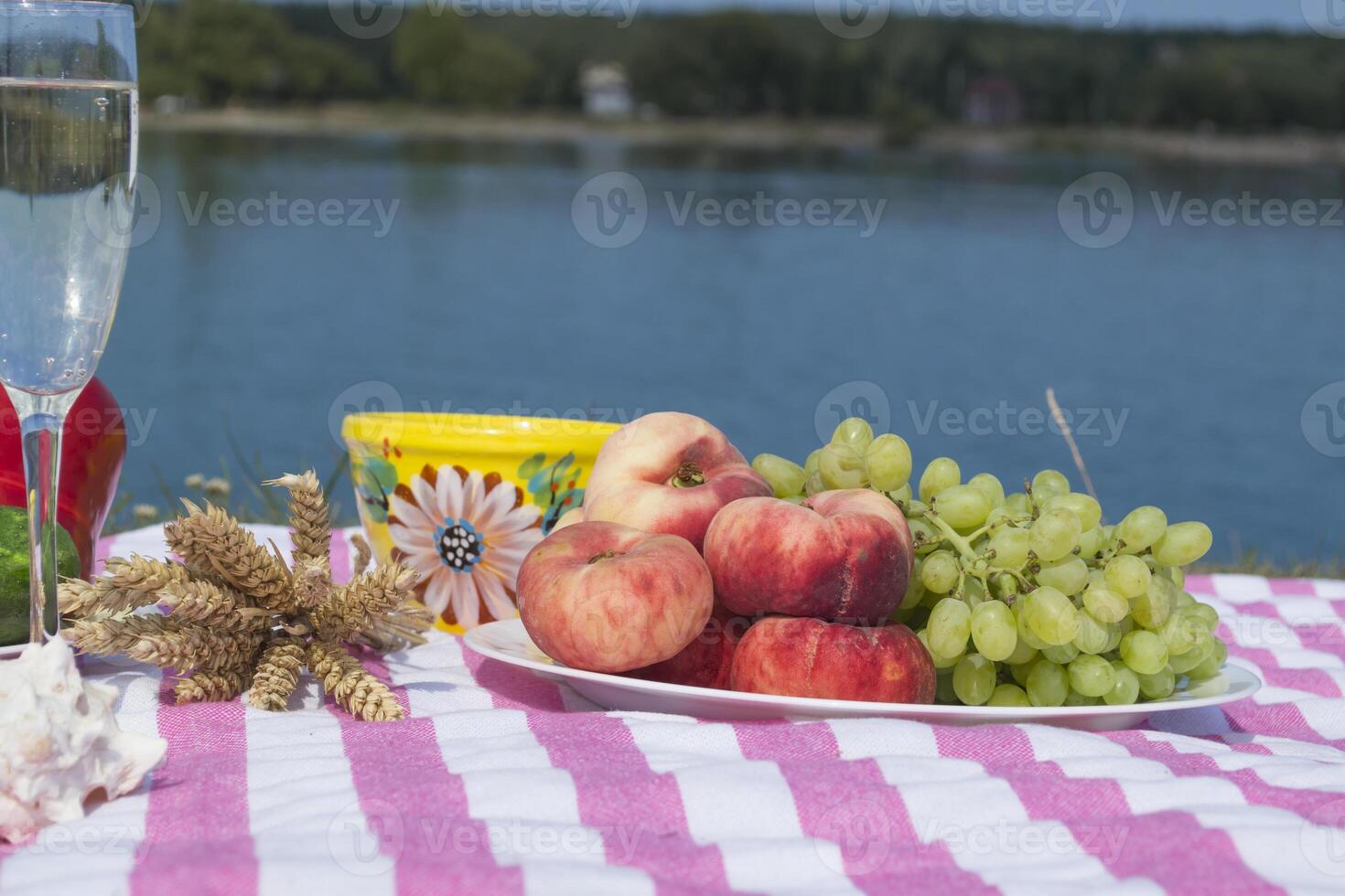Beautiful picnic with fruits, vegetables and glasses of wine near lake. photo