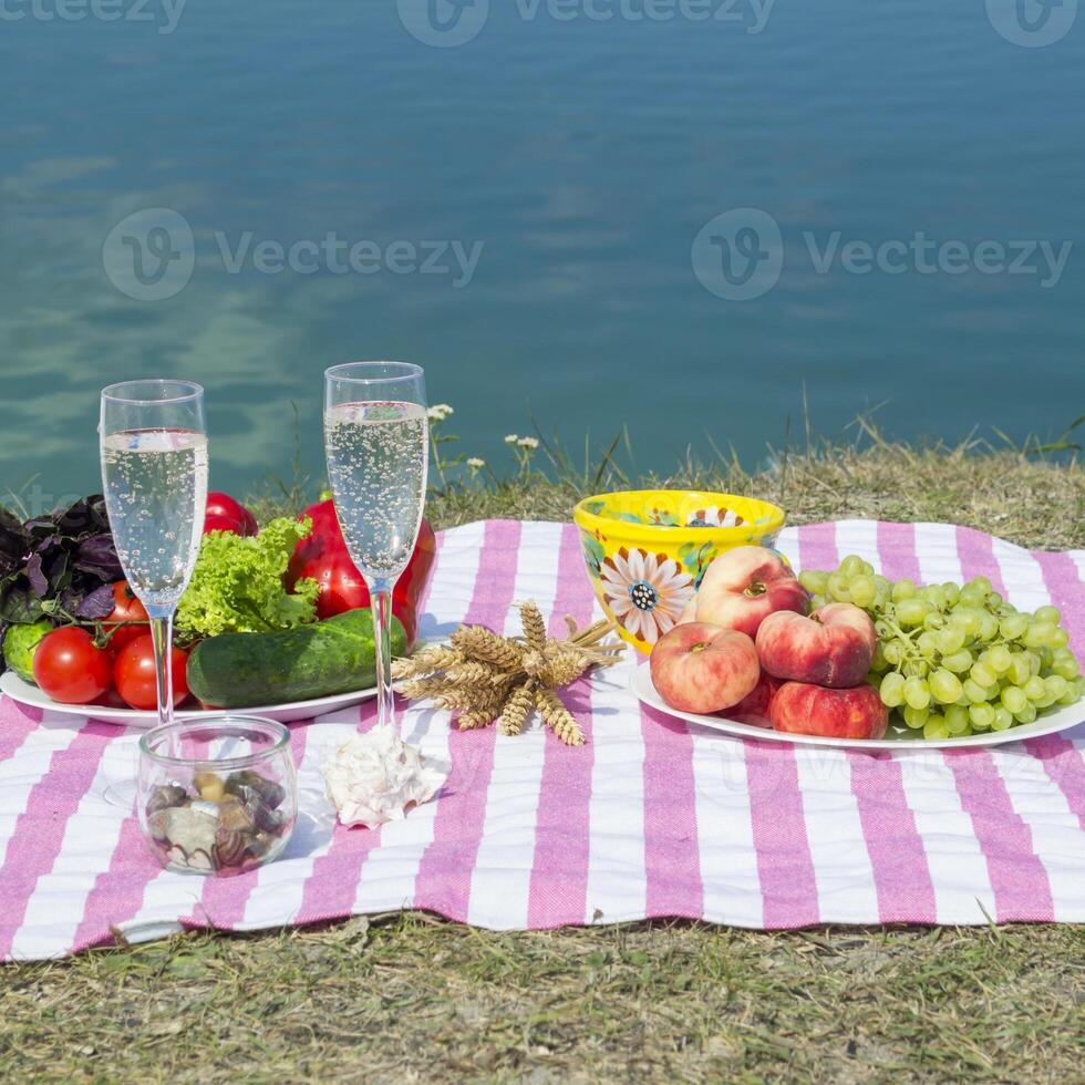 hermosa picnic con frutas, vegetales y lentes de vino cerca lago. foto